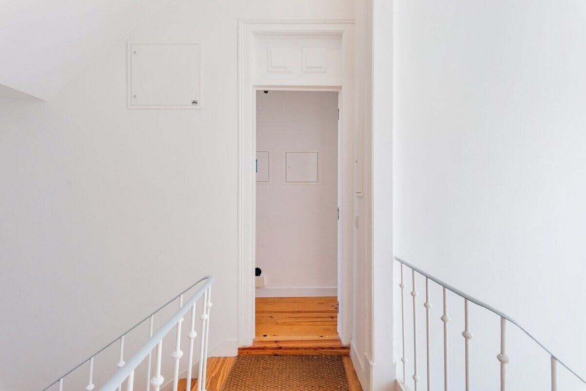 A narrow hallway with white walls, a wooden floor, and a white railing.