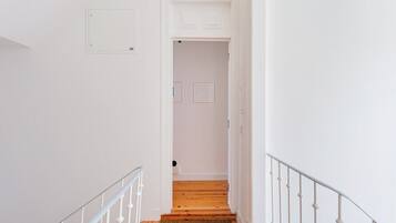 A narrow hallway with white walls, a wooden floor, and a white railing.