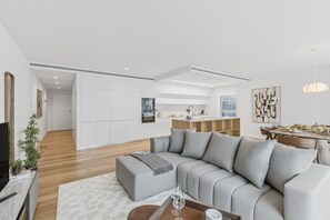 Ein modernes Wohnzimmer mit einer grauen Eckcouch, einem Couchtisch und einem Essbereich mit Holztisch und Stühlen.