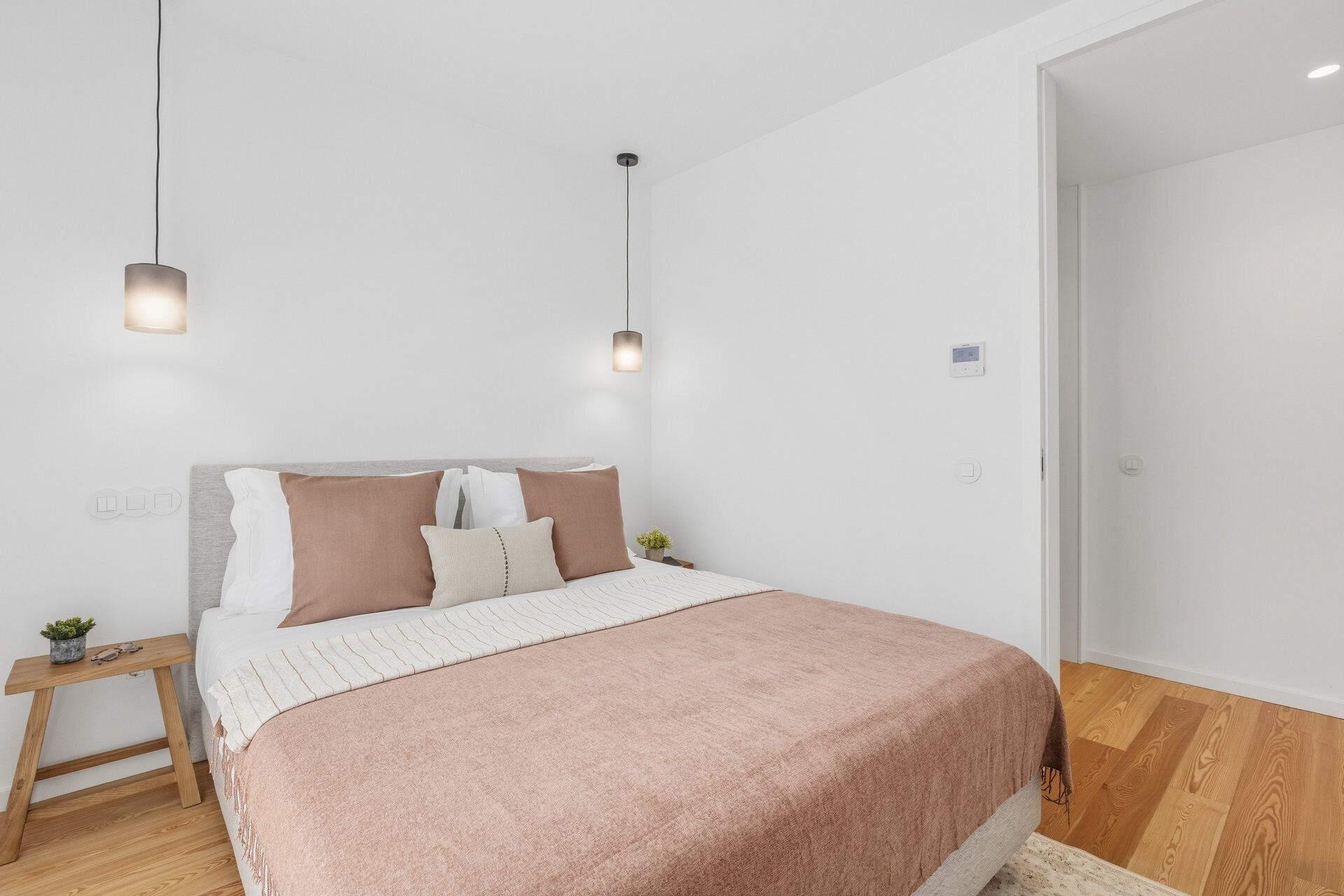 A bedroom with a bed, bedside tables, a nightstand, a wall-mounted thermostat, and a door.