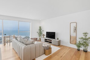 Ein modernes Wohnzimmer mit großem Fenster, einer Couch, einem Fernseher und einem Spiegel.