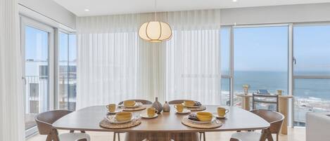 A dining room with a round table, chairs, and a view of the ocean.