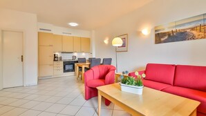 Een moderne woonkamer met een rode bank, een houten salontafel met een plant, een eethoek met een tafel en stoelen, en een keuken op de achtergrond.