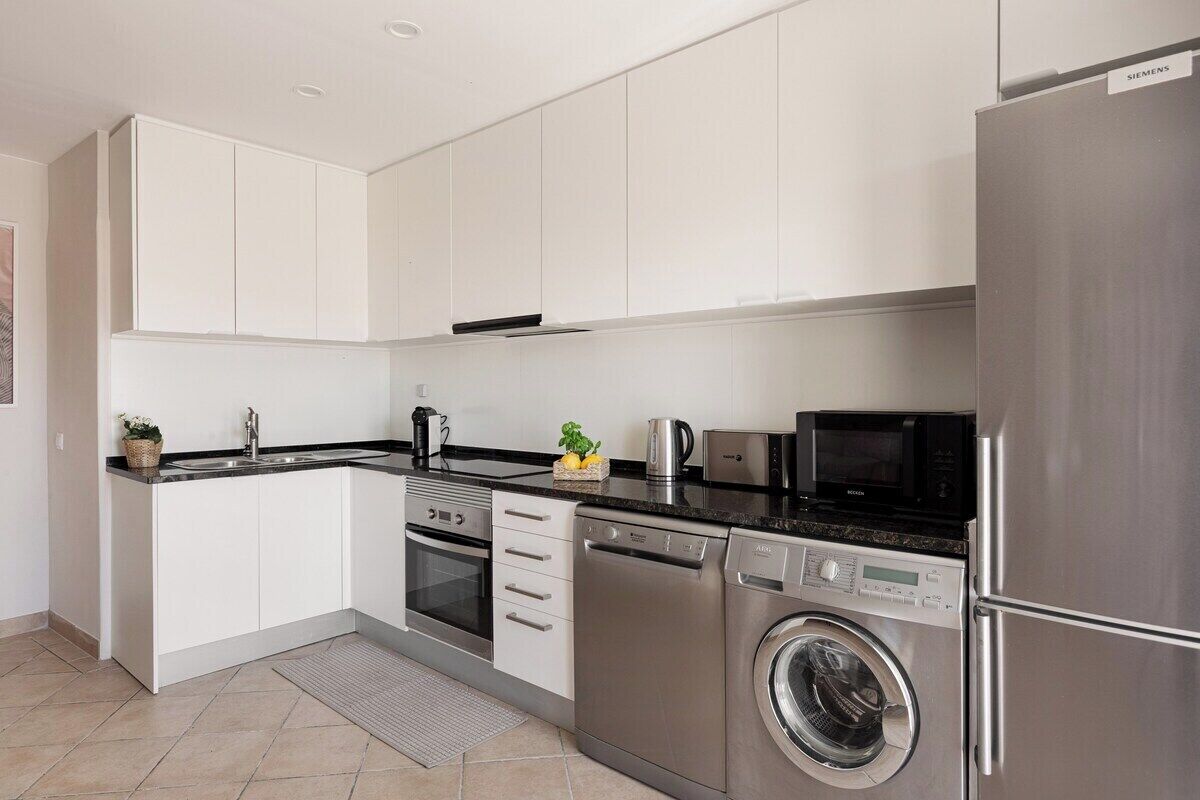 A modern kitchen with white cabinets, stainless steel appliances, and a built-in washing machine.