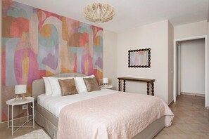 Ein Schlafzimmer mit einem großen Bett, einem Nachttisch, einer Lampe, einem Wandbild und einem Spiegel.