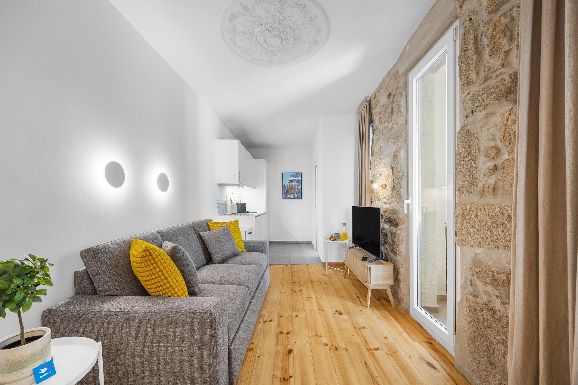 Uma sala de estar moderna com sofá cinzento, piso de madeira, televisão e parede de pedra.
