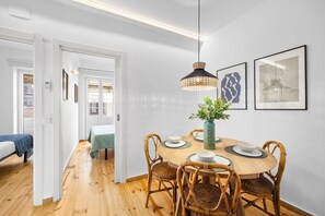 Uma área de refeições com uma mesa de madeira redonda, cadeiras de vime, uma luminária pendente e quadros nas paredes.