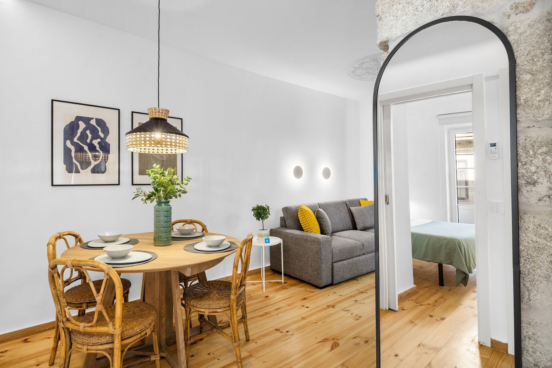 Een eetgedeelte met een ronde tafel, rieten stoelen, een hanglamp en een bank op de achtergrond.