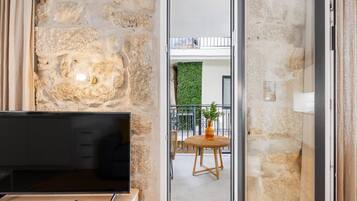 Een kamer met een stenen muur, een televisie op een houten standaard, een afstandsbediening, en een balkon met een rieten stoel en een vaas.