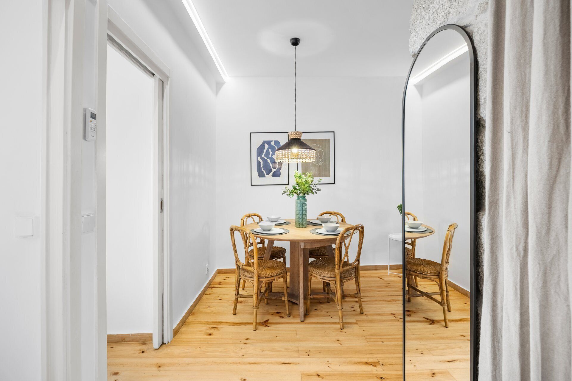 Een eethoek met een ronde tafel, zes rieten stoelen, een centraal vaasje en een hanglamp.