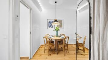Een eethoek met een ronde tafel, zes rieten stoelen, een centraal vaasje en een hanglamp.