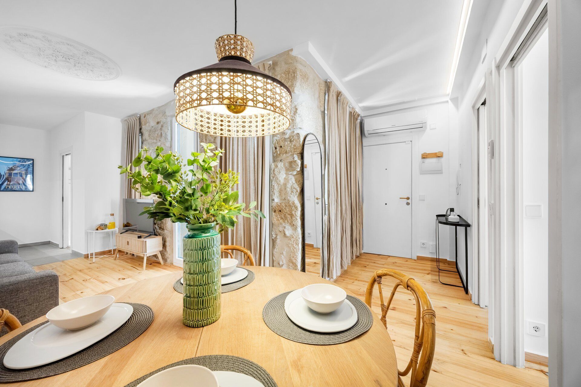 Un coin repas avec une table en bois, des chaises, un luminaire suspendu et un vase vert contenant des plantes.