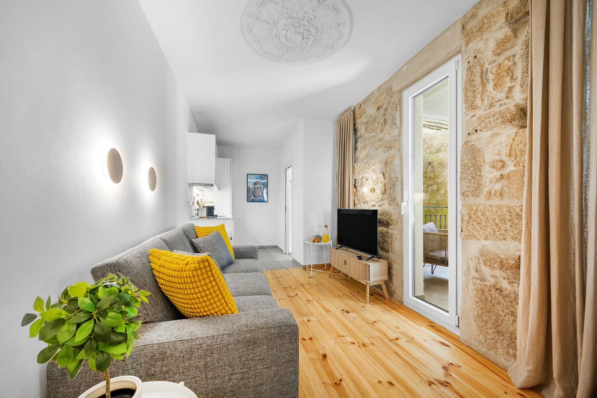 Un salon moderne avec un canapé gris, des coussins jaunes, un téléviseur et un mur en pierre.