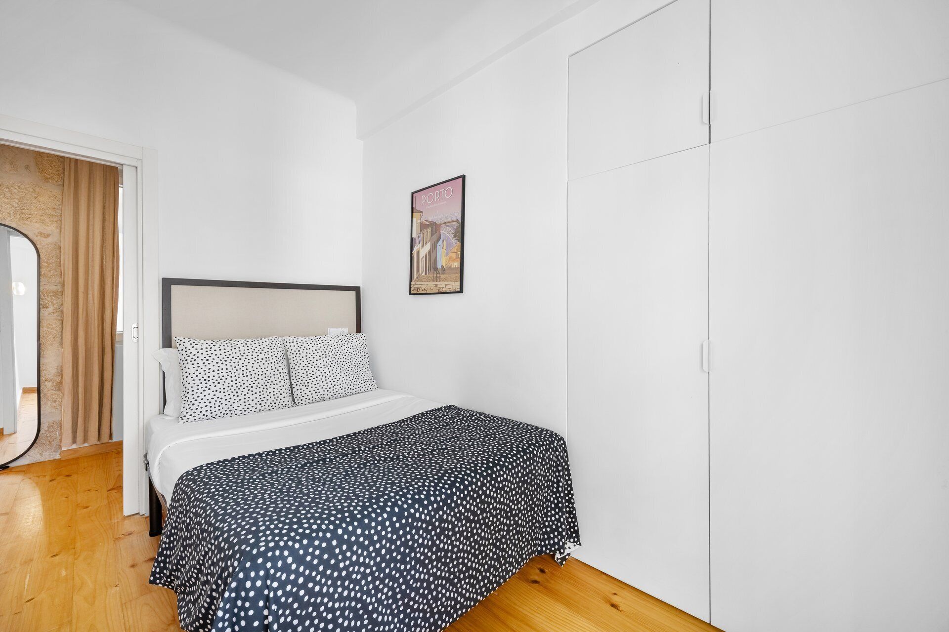 A bedroom with a bed, a wardrobe, a door, and a wall-mounted picture.