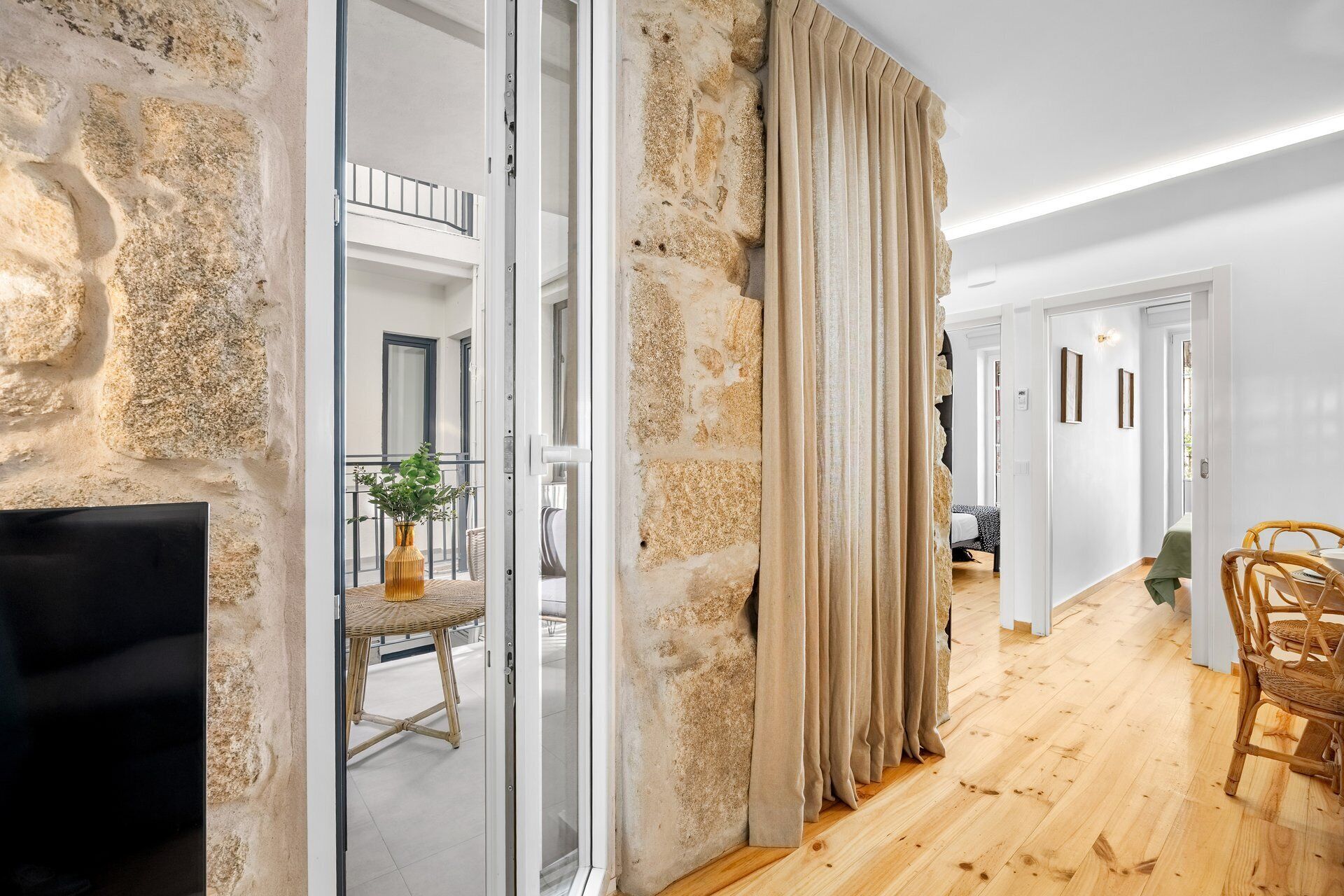 Una habitación con pared de piedra, puerta de cristal, silla de mimbre y televisor de pantalla plana.