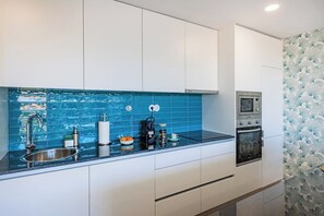 A modern kitchen with white cabinets, a blue backsplash, a stainless steel sink, a built-in oven, and a microwave. - Espinho Sunny Vibes & Balcony with Pool (Espinho)