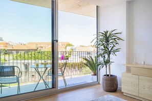 A balcony with a view of buildings, a potted plant, a table with chairs, and a wooden cabinet. - Espinho Sunny Vibes & Balcony with Pool (Espinho)