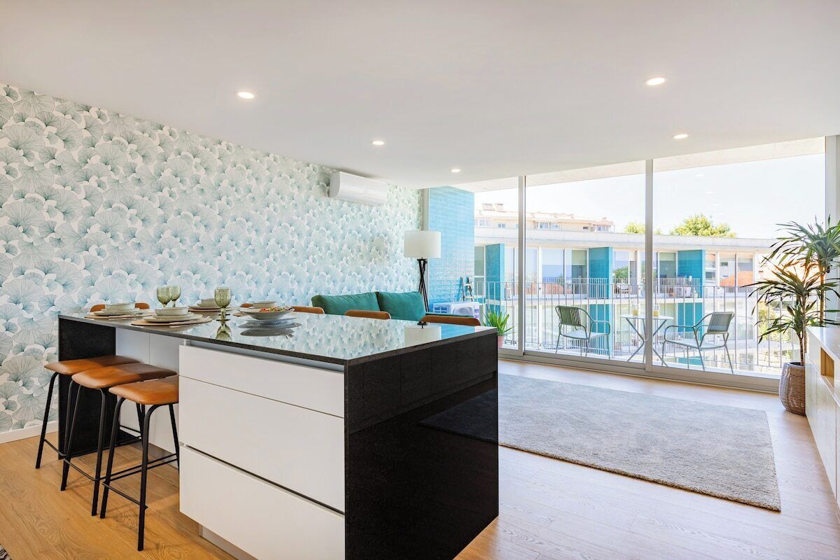 A modern kitchen with a central island, bar stools, and a view to the outside.