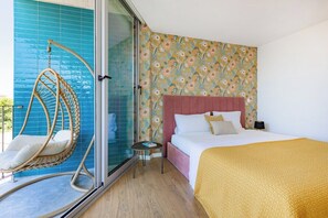 A hotel room with a bed, a hanging chair, a small table, and a window with blue-tiled walls. - Espinho Sunny Vibes & Balcony with Pool (Espinho)