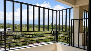 A balcony with a metal railing, a view of a green landscape, and a building in the distance.