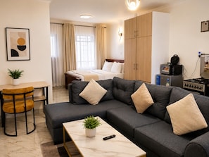 Una habitación de hotel moderna con sofá, una mesita, cama, escritorio y kitchenette.