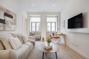 A modern living room with a sofa, coffee table, TV, and windows. - The Soft Escape @ BoaVista Flats (Porto)