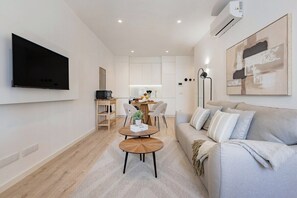 Ein modernes Wohnzimmer mit Flachbildfernseher, einer Couch, einem Essbereich mit Stühlen und einer Küche im Hintergrund.