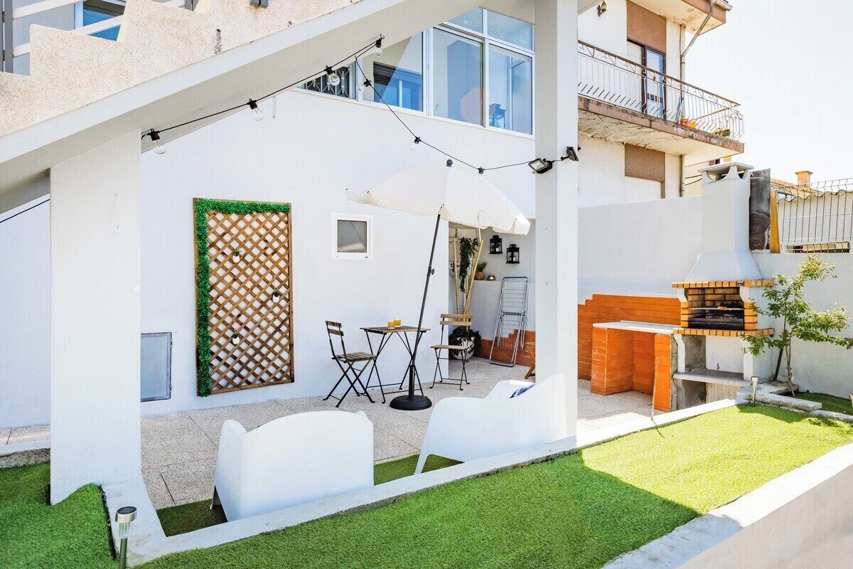Eine moderne Terrassenanlage mit Grill, weißen Stühlen und einem kleinen Tisch.