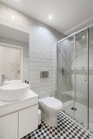 A modern bathroom with a white sink, toilet, and glass shower enclosure. - Lapa Design Studio with Workspace (Porto)