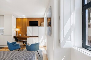 Ein modernes Hotelzimmer mit Küchenzeile, einem Esstisch mit Stühlen und einem großen Fenster.