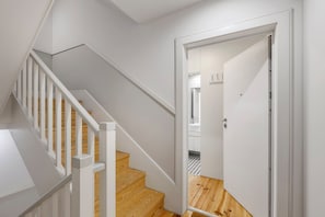 Eine Treppe mit weißen Geländern und Holzstufen führt zu einem Raum mit einer weißen Tür und einem Schachbrettfußboden.