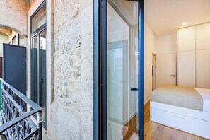 A bedroom with a stone wall, a sliding glass door, a bed, and a wardrobe. - Netto City Vibes (Porto)
