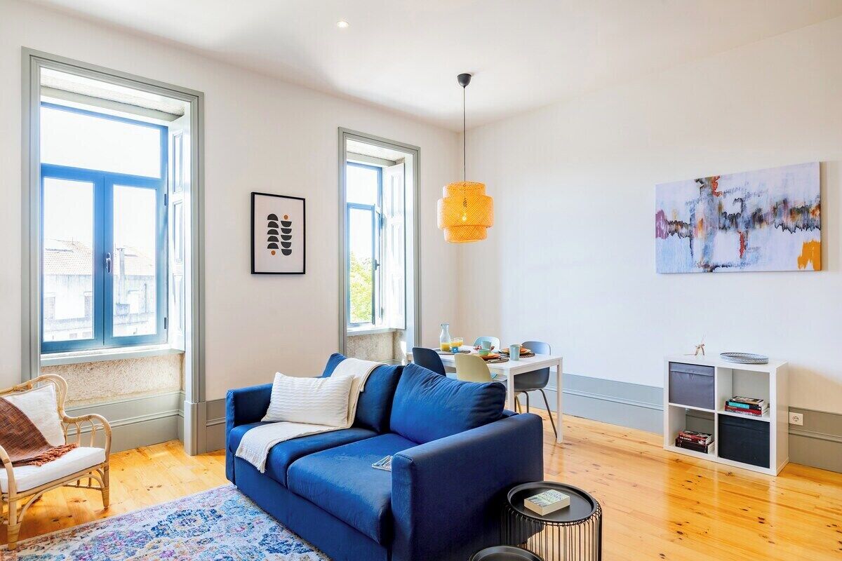 Ein modernes Wohnzimmer mit einem blauen Sofa, einem Korbstuhl, einem Esstisch und einem Bücherregal.