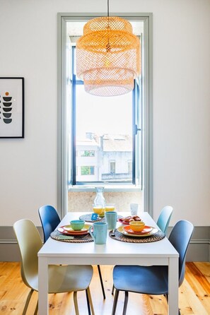 A dining area with a table set for two, a hanging orange pendant light, and a window with a view of buildings. - Boavista Light Studio (Porto)