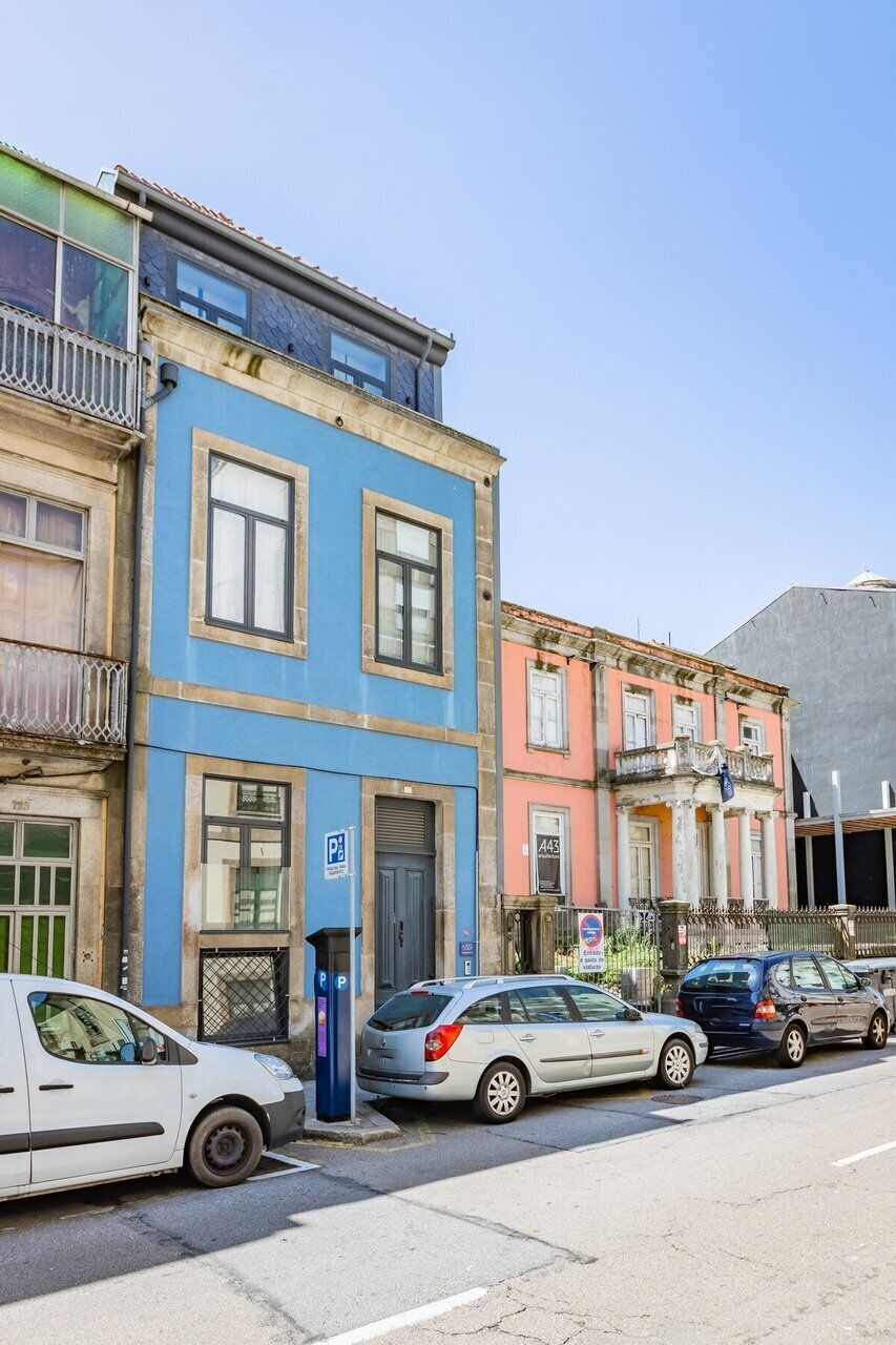 Een straat met geparkeerde auto's, een blauw gebouw met een deur en een roze gebouw met kolommen.