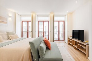 Ein Schlafzimmer mit einem Bett, einem Schlafsofa, einem Fernseher und einem Balkon mit Geländer.