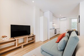 Ein modernes Wohnzimmer mit Flachbildfernseher, einer Couch und einem Küchenbereich im Hintergrund.
