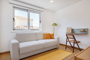 Ein Zimmer mit einer Couch, einem Sessel, einer Lampe und einem Fenster.