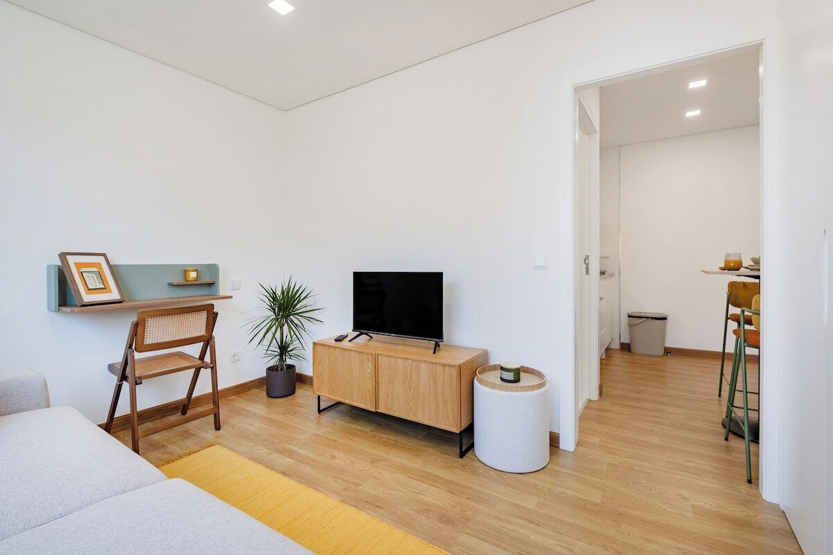 Un salon moderne avec un canapé, un meuble TV en bois, une plante en pot et une petite table sur laquelle est posée une bougie.