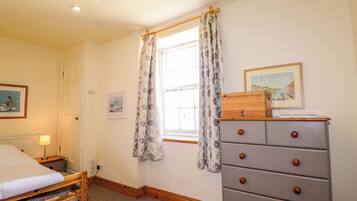 Un dormitorio con cama, cómoda, ventana con cortinas y dos cuadros en la pared.