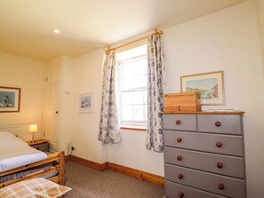 Ein Schlafzimmer mit einem Bett, einem Schminktisch, einem Fenster mit Vorhängen und zwei gerahmten Bildern an der Wand.