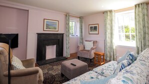 A living room with a fireplace, a sofa, a chair, a small table, and two windows with curtains. - 6 Hill Street (Banff)