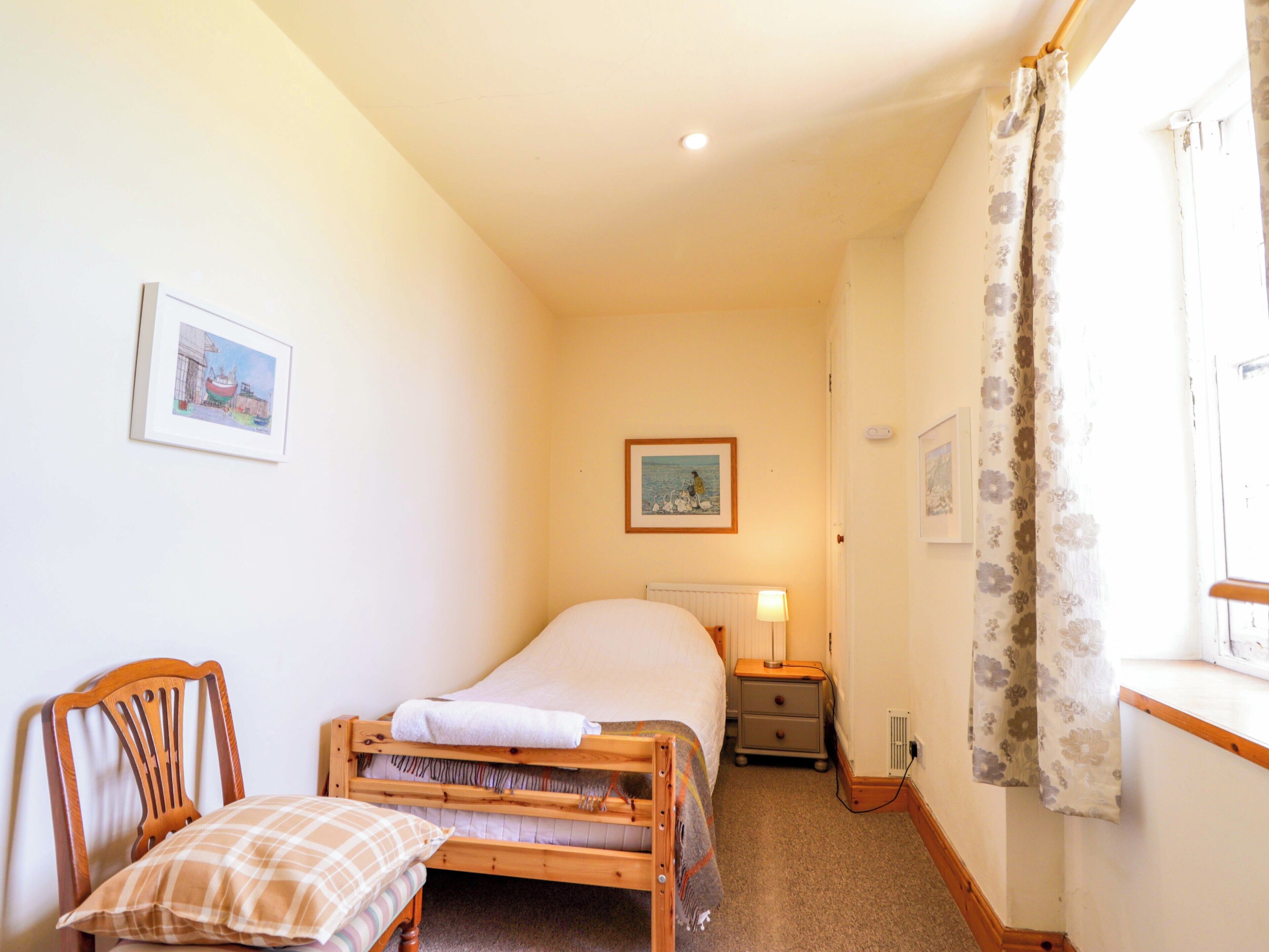A bedroom with a bed, a chair, a nightstand, a lamp, and two framed pictures on the wall.