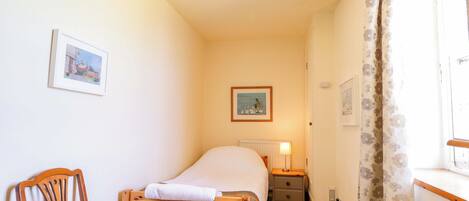 A bedroom with a bed, a chair, a nightstand, a lamp, and two framed pictures on the wall.