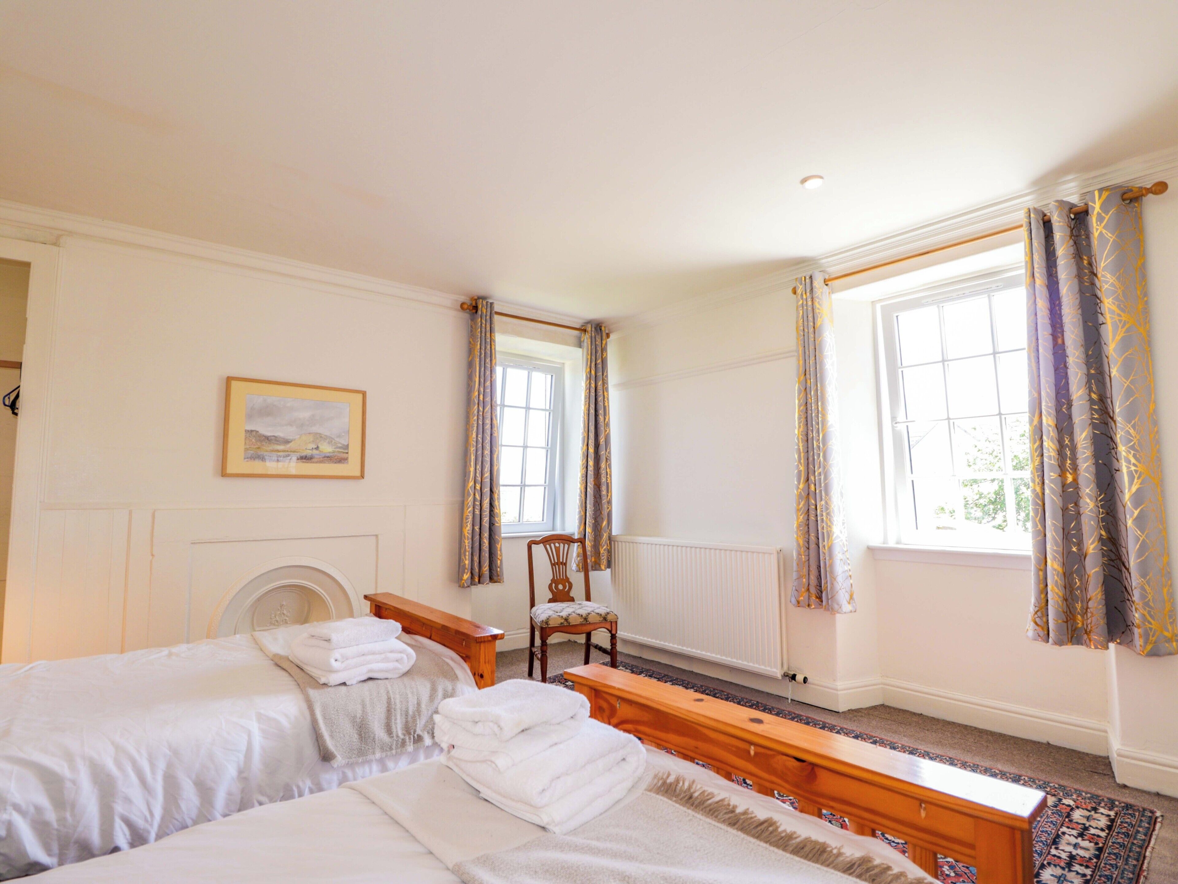 Ein Schlafzimmer mit zwei Betten, einem Sessel, einem Heizkörper und einem Fenster mit Vorhängen.