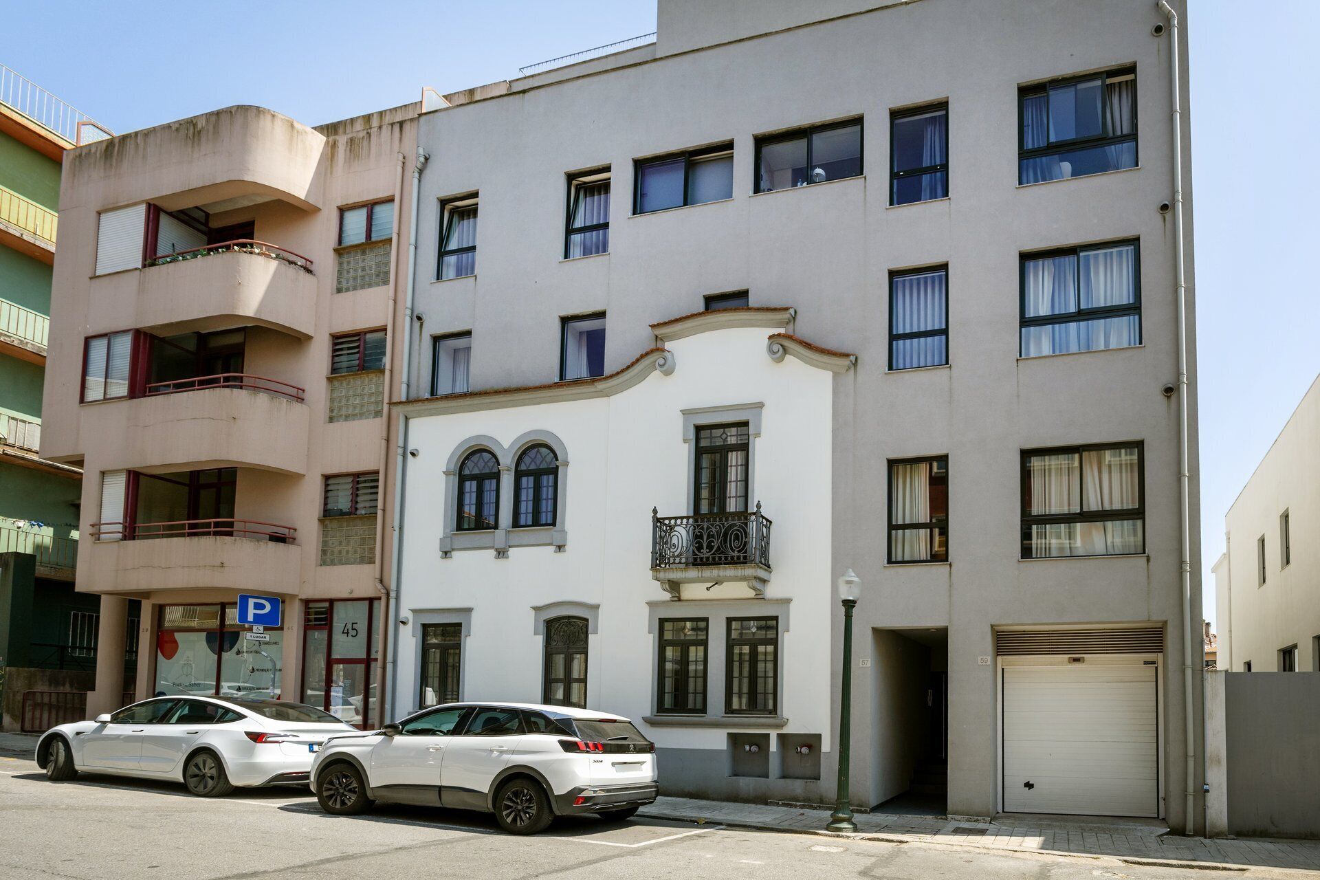 En byggnad med flera våningar, en parkeringsskylt, två parkerade bilar och en garageport.