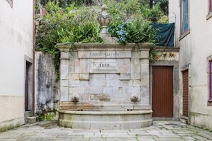 A stone fountain with inscriptions, surrounded by greenery and a door. - CharmINN Paraíso | Porto | AC (Porto)