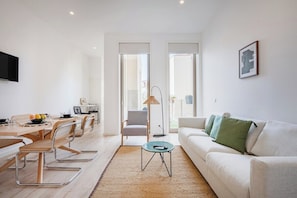 A modern living room with a sofa, a dining table with chairs, a coffee table, and a TV mounted on the wall. - The Superior Green @ BoaVista Flats (Porto)