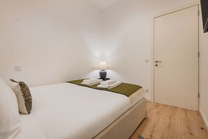 Ein Einzelbett mit grüner Decke, einer Nachttischlampe und einem gefalteten Handtuch.