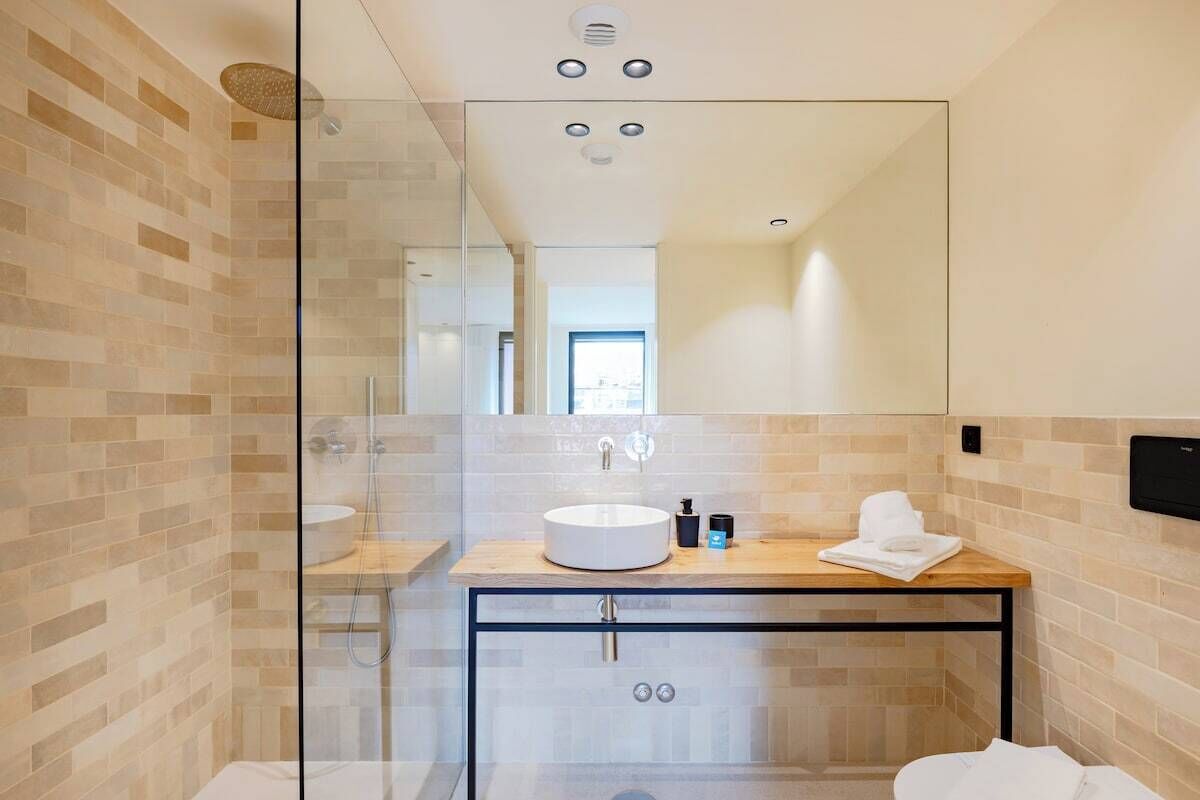 Een moderne badkamer met een glazen douchecabine, een rond wastafeltje en een houten aanrechtblad.